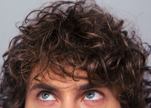 Man with full head of hair looking upward on a gray background