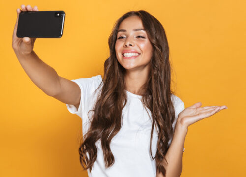 Brunette woman taking a selfie and smiling on a yellow background