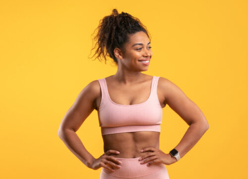 Fit gym woman with hands on hips on a yellow background