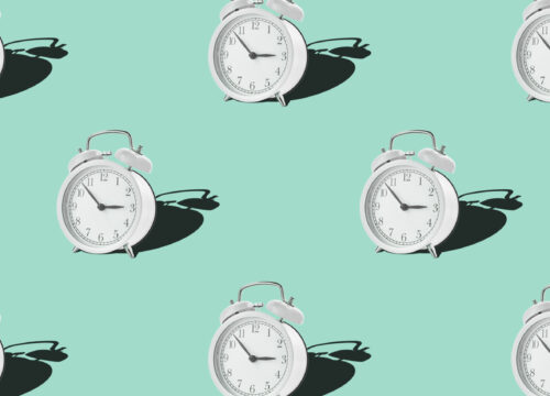 Multiple white alarm clocks on a mint green background