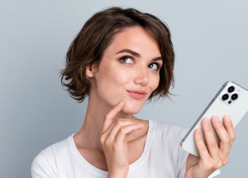 Brunette woman on gray background holding a cell phone
