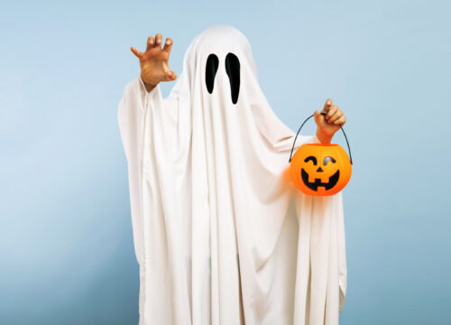 Person in a ghost costume for Halloween holding a pumpkin bucket on a blue background