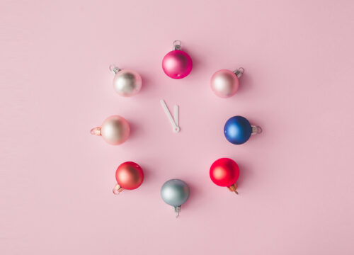 Holiday bulbs forming a clock on a light pink background
