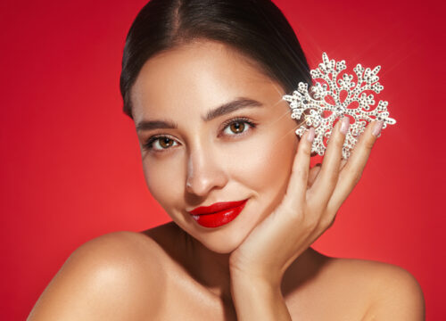 Brunette woman with red lips and glowing skin holding a snowflake on a red background