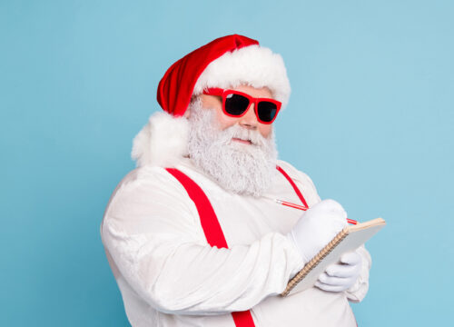 Santa in sunglasses making his nice list while standing in front of a light blue background