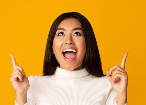 Brunette woman with white sweater pointing upwards on a golden background