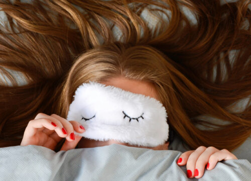 Woman in bed with sleeping mask over eyes and thick hair draped over her pillow