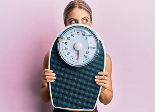 Blonde woman holding a scale in front of her on a pink background