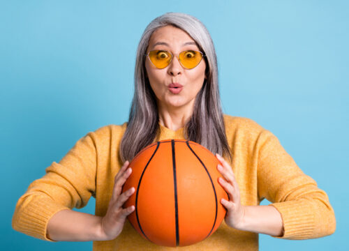 Woman with grey hair and sunglasses holding a basketball on a blue background