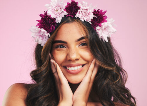Brunette woman wearing a flower crown with a pink background behind her