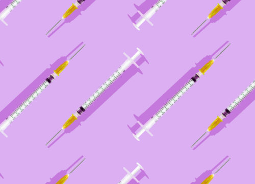 Multiple injectable syringes laid out on a bright pink-purple background